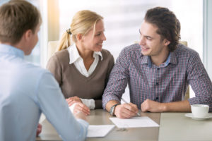 Young smiling couple about to sign a house renting agreement, happy to buy new apartment, meeting in the office with a trusted, reliable real estate agent, confident in credit